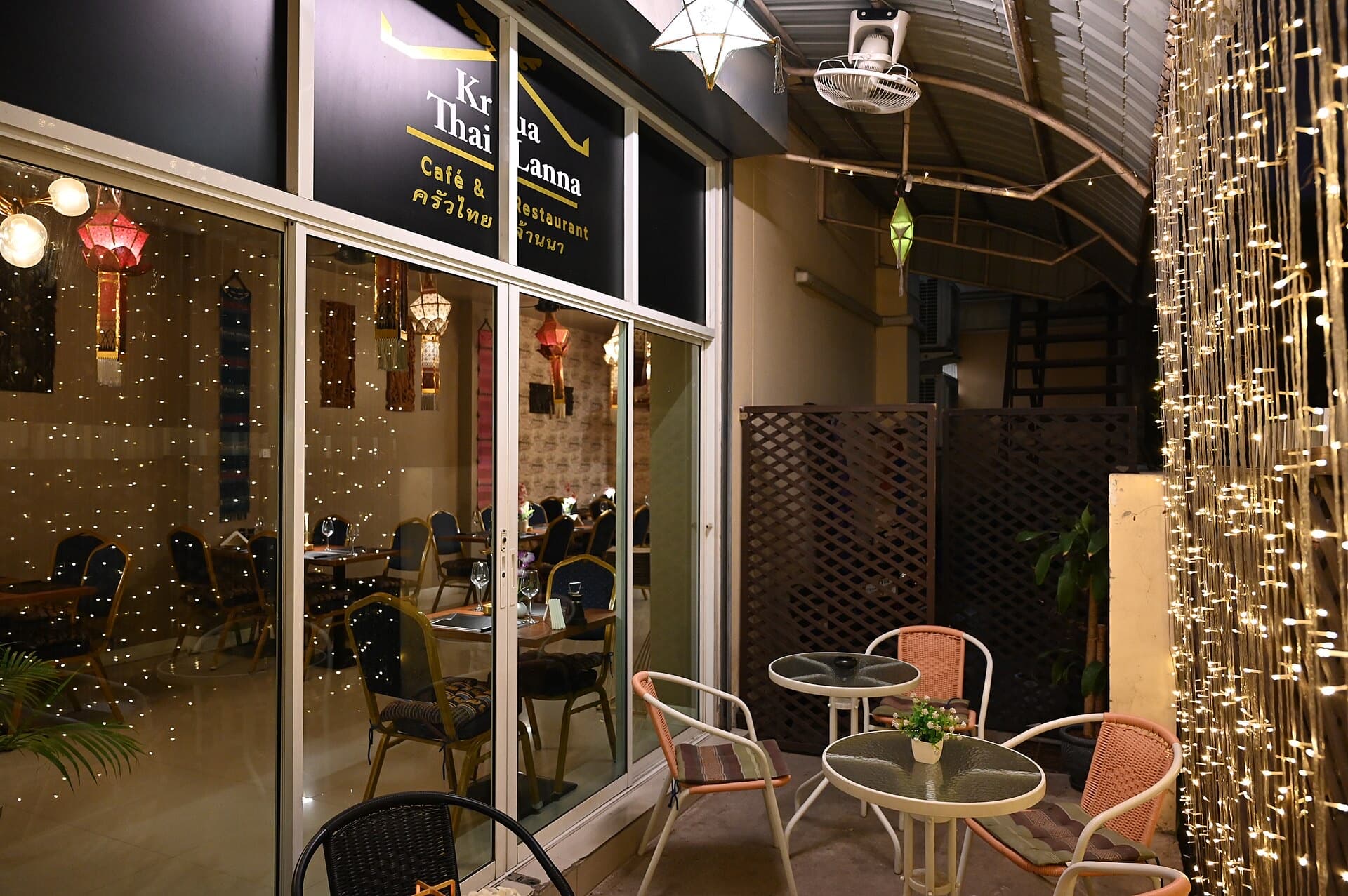 Terraza de un café de noche, con mesas, sillas y cortinas de luces